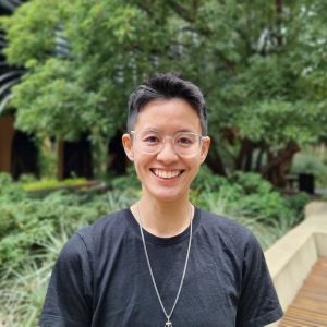 Profile headshot of CEBRA Research Fellow Meryl Theng in a campus garden. Meryl has short, black hair and is wearing a black t-shirt